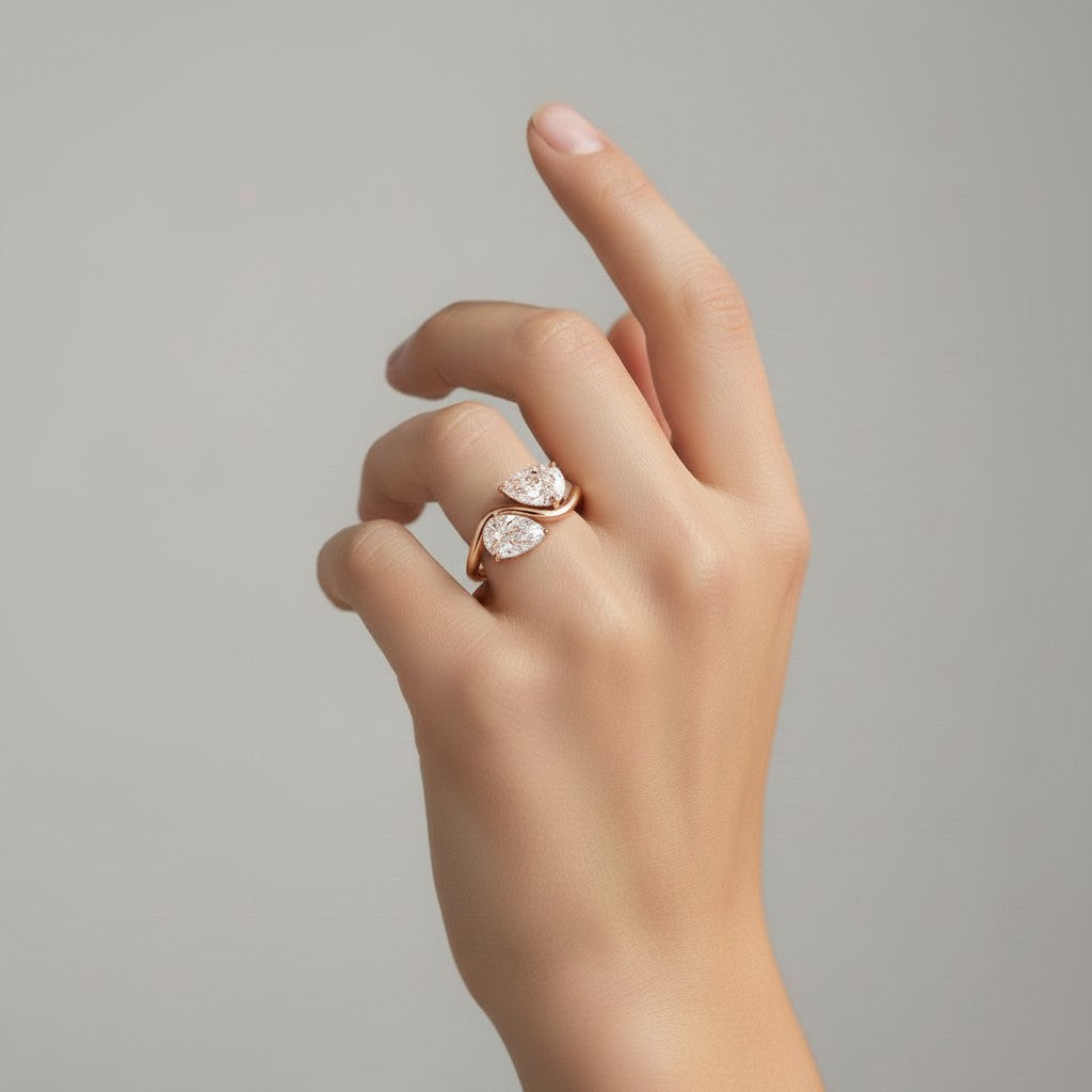 My Store 4 bypass engagement ring with two pear-cut diamonds on a polished rose gold S-curve band worn on a finger.