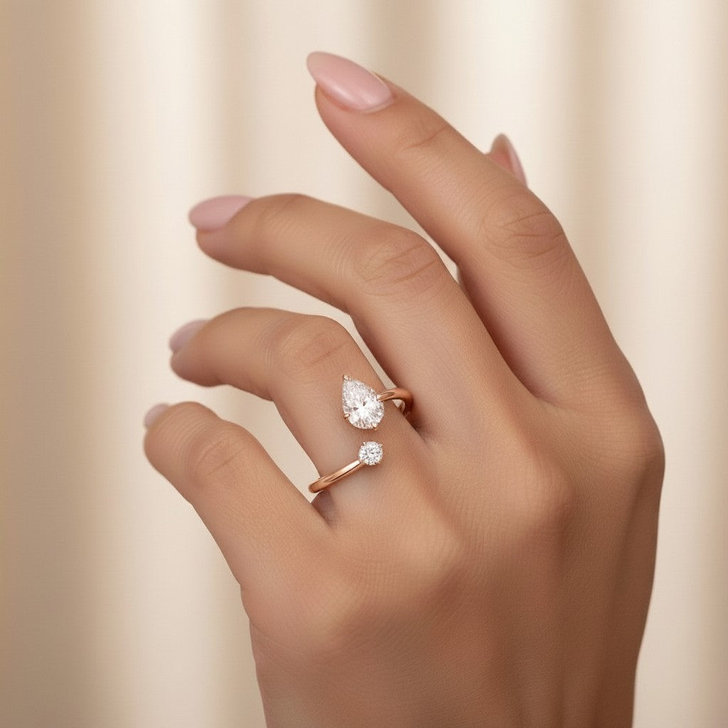 My Store 4 bypass engagement ring featuring a pear-cut and round-cut diamond on a solid gold open band on a finger.