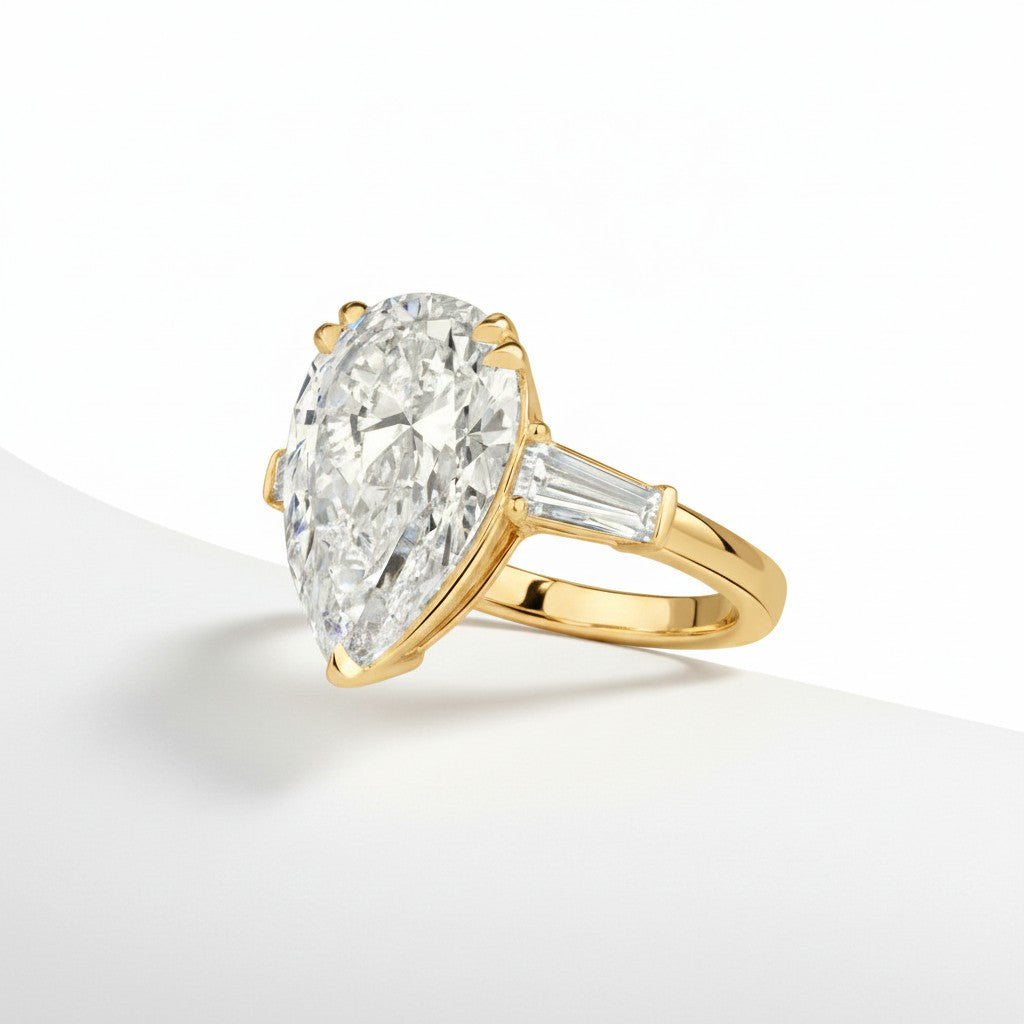 My Store 4 pear cut engagement ring with tapered baguette side diamonds in polished yellow gold on a white surface.