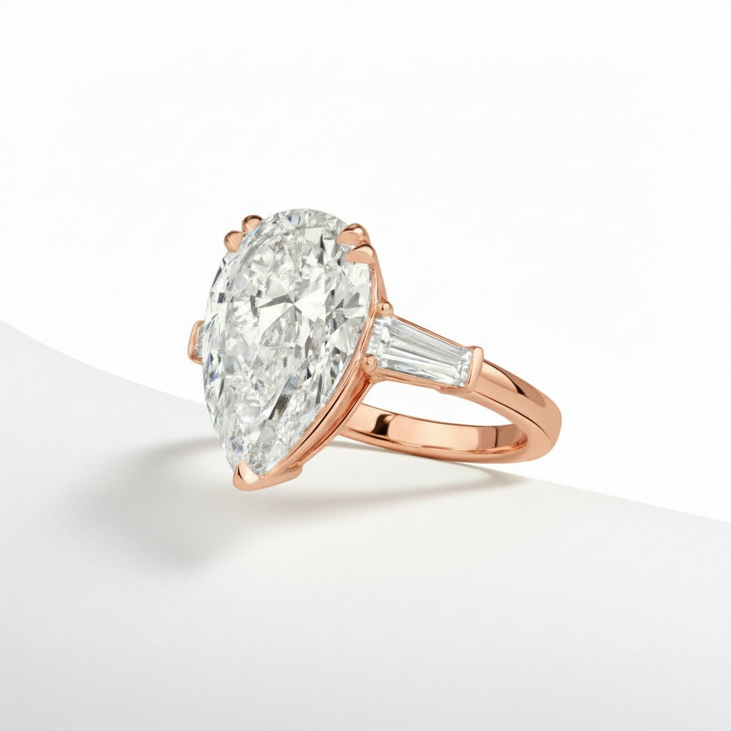 My Store 4 pear cut engagement ring with tapered baguette side diamonds in polished rose gold on a white surface.