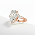 My Store 4 pear cut engagement ring with tapered baguette side diamonds in polished rose gold on a white surface.