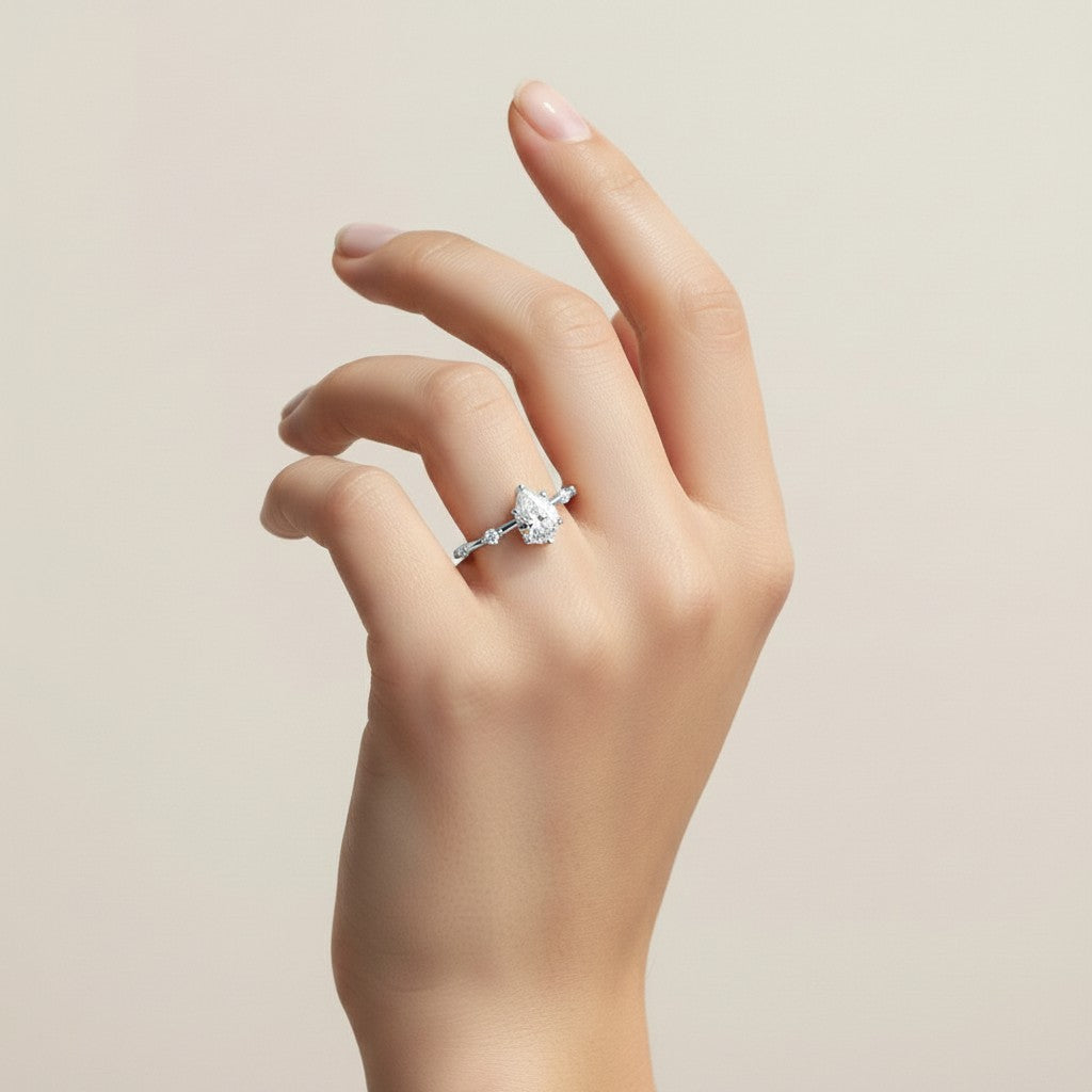 My Store 4 pear cut diamond engagement ring with a station accent band on a model hand against a neutral background.