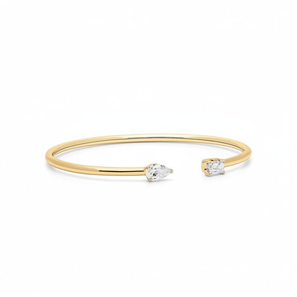 My Store 4 open cuff bracelet in yellow gold with a pear-cut diamond on one end and an emerald-cut diamond on the other.
