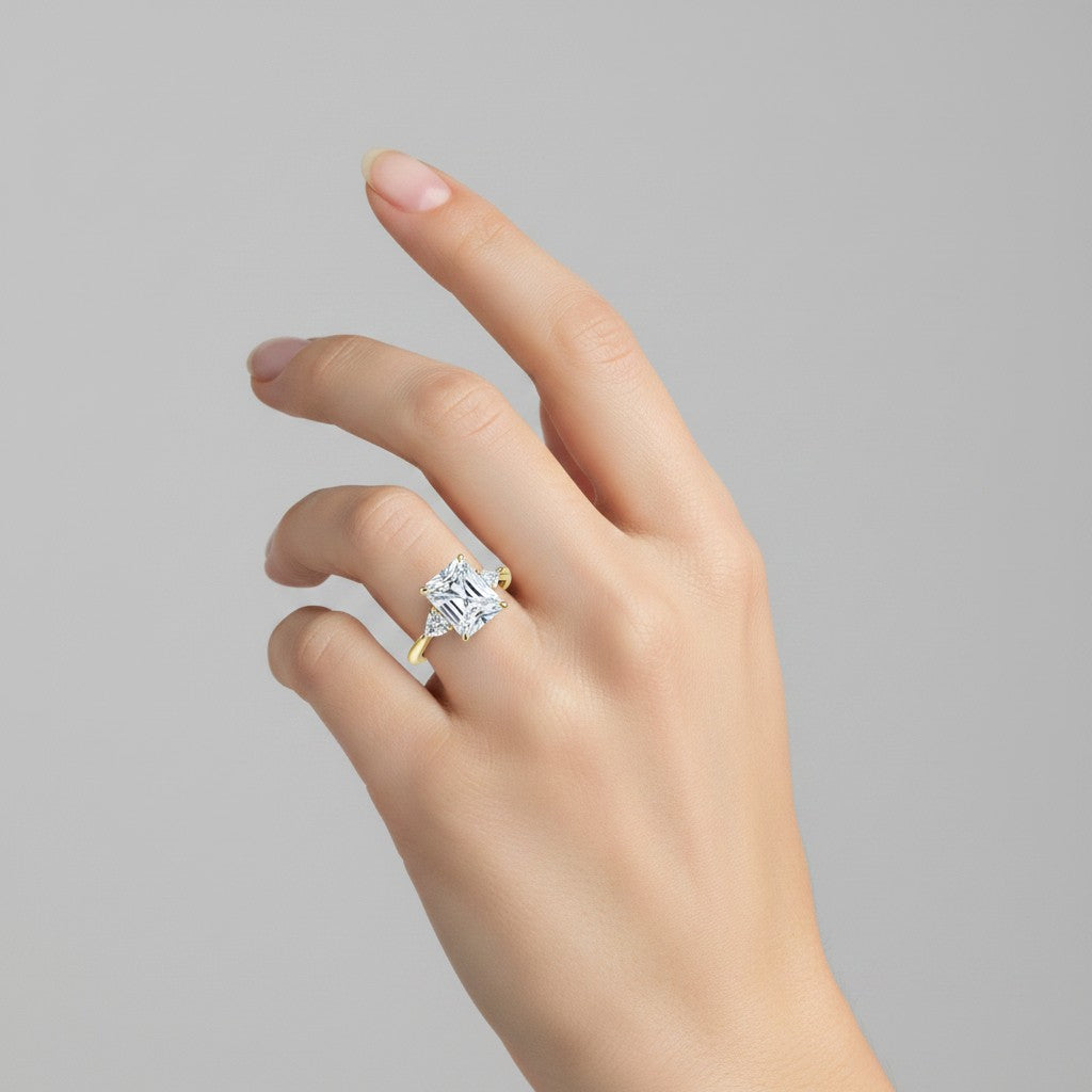 My Store 4 radiant cut three-stone engagement ring with trillion side diamonds on a yellow gold band worn on a finger