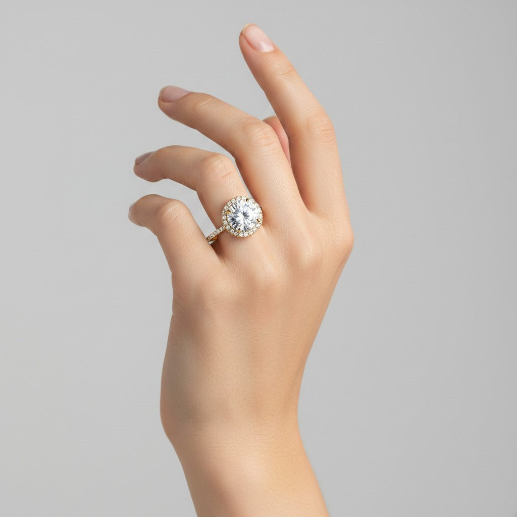 My Store 4 round cut halo engagement ring with pavé diamonds on a yellow gold band worn on a woman's hand